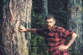 Tall brutal man standing in forest. Lumberjack resting while leaning on tree. Hipster with roses tattoo on arm Royalty Free Stock Photo