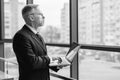 Bearded man standing near window with laptop. Panoramic city view. Black and white photo. Royalty Free Stock Photo