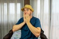 Bearded man in a straw hat dressed in a dark blue shirt with a shocked expression in the living room at home Royalty Free Stock Photo