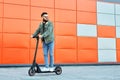 Bearded man in sunglasses posing on electric scooter over orange wall background. Man riding kick scooter. Royalty Free Stock Photo