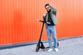 Bearded man in sunglasses posing on electric scooter over orange wall background. Man riding kick scooter. Royalty Free Stock Photo