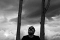 Bearded man with sunglasses sitting in front two trees and stormy sky, looking up, contemplating Royalty Free Stock Photo