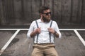 Bearded man in sunglasses and suspenders sitting on parking and looking away