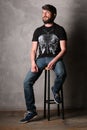 Bearded man in T-shirt with butterfly sitting on a bar stool. Gray