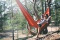 Bearded man traveller in felt hat rests alone in tourist hammock in sunny pine forest enjoying his loneliness, sense of peace and