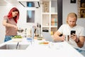 Bearded man using cellphone while his girlfriend cooking in kitchen Royalty Free Stock Photo