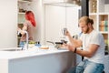 Bearded man using cellphone while his girlfriend cooking in kitchen Royalty Free Stock Photo
