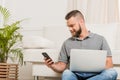 Bearded man using laptop and smartphone while sitting on sofa at home Royalty Free Stock Photo