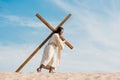 Bearded man walking with wooden cross against sky Royalty Free Stock Photo
