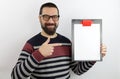 Bearded man wearing eyeglasses wearing casual clothes holding a clipboard with a blank paper pointing with his finger to the side Royalty Free Stock Photo