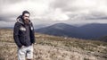 Bearded man on windy mountain top on natural cloudy sky