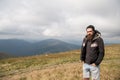 Bearded man on windy mountain top on natural cloudy sky