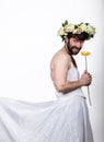 Bearded man in a woman`s wedding dress on her naked body, holding a flower. on his head a wreath of flowers. funny Royalty Free Stock Photo