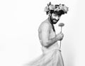 Bearded man in a woman`s wedding dress on her naked body, holding a flower. on his head a wreath of flowers. funny Royalty Free Stock Photo