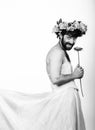 Bearded man in a woman`s wedding dress on her naked body, holding a flower. on his head a wreath of flowers. funny Royalty Free Stock Photo