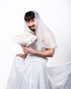 Bearded man in a woman`s wedding dress on her naked body, holding a flower. on his head a wreath of flowers. funny Royalty Free Stock Photo