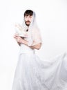 Bearded man in a woman`s wedding dress on her naked body, holding a flower. on his head a wreath of flowers. funny Royalty Free Stock Photo