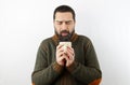 Bearded man with woolen sweater on white background blows on cup of hot tea holding in hands Royalty Free Stock Photo