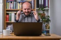 Bearded man working online from home on computer laptop behind vintage desk, with earphones