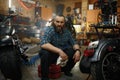 Bearded mature man biker cleaning motorcycle in garage workstation