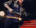 Mechanic cuts steel car part with an angle grinder.