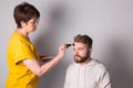 Bearded man getting makeup. Woman visagist works with brush.