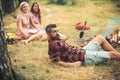 Bearded man in lumberjack shirt lying on grass, unity with nature concept. Group of young hikers camping in forest Royalty Free Stock Photo