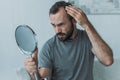 bearded middle aged man with alopecia looking at mirror hair loss