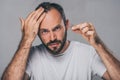 bearded middle aged man holding fallen hair and looking at camera