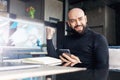 Bearded middle-aged man holds smartphone and is emotionally happy about winning, winning while sitting in cafe at table