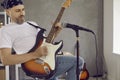 Male guitarist playing riff on his electric guitar in modern studio with microphone