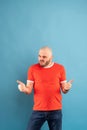 A bearded middle-aged man in a red T-shirt on a blue background rejoices and shows his thumbs up. Isolated Royalty Free Stock Photo