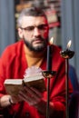 Bearded mysterious diviner reading book near flaming candles