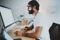 Bearded professional architect wearing eye glasses and white tshirt working at modern loft studio-office with desktop