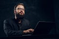 A bearded programmer sitting at the table with laptop in office against a dark wall
