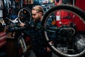 Bearded repairman repairing mountain bicycle on bike rack working in bicycle repair shop with dark interior. Male Royalty Free Stock Photo