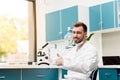 Bearded scientist in lab coat showing thumb up while working with microscope in lab