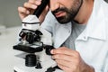 Bearded scientist in white coat working with microscope in lab