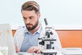 Bearded scientist working with microscope and laptop in laboratory