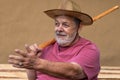 Man in straw hat sitting against clay wall, gesticulating with left hand while  holding wicker walking stick in right one o Royalty Free Stock Photo