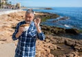 A bearded senior stands on the Mediterranean shore in Spain and shows a kebab.
