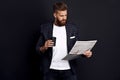 Bearded smart handsome concentrated chief dressed in jacket and shirt reading latest news from newspaper and drinking coffee Royalty Free Stock Photo