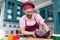 Bearded smiled chef hold two parts of red cabbage at kitchen. Cook cut red cabbage for two parts.