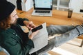 Bearded student sits with his feet up on his desk while studying online using laptop and smartphone
