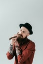 bearded tattooed man shaving beard with razor