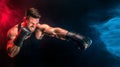 Bearded tattooed sportsman muay thai boxer in black undershirt and boxing gloves fighting on dark background with smoke.