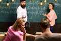 Bearded teacher, lecturer, professor watching students during test, exam, lesson. Students, group mates speaking, asking Royalty Free Stock Photo