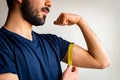 Bearded thin man measuring biceps, muscles of his left arm with a yellow tape measure. He`s calm, serious, quiet. Royalty Free Stock Photo