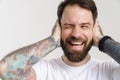 Bearded white man with tattoo laughing and covering his ears