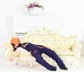 Bearded worker sleeping on sofa in white room with protective helmet covering his face. Builder enjoying break and